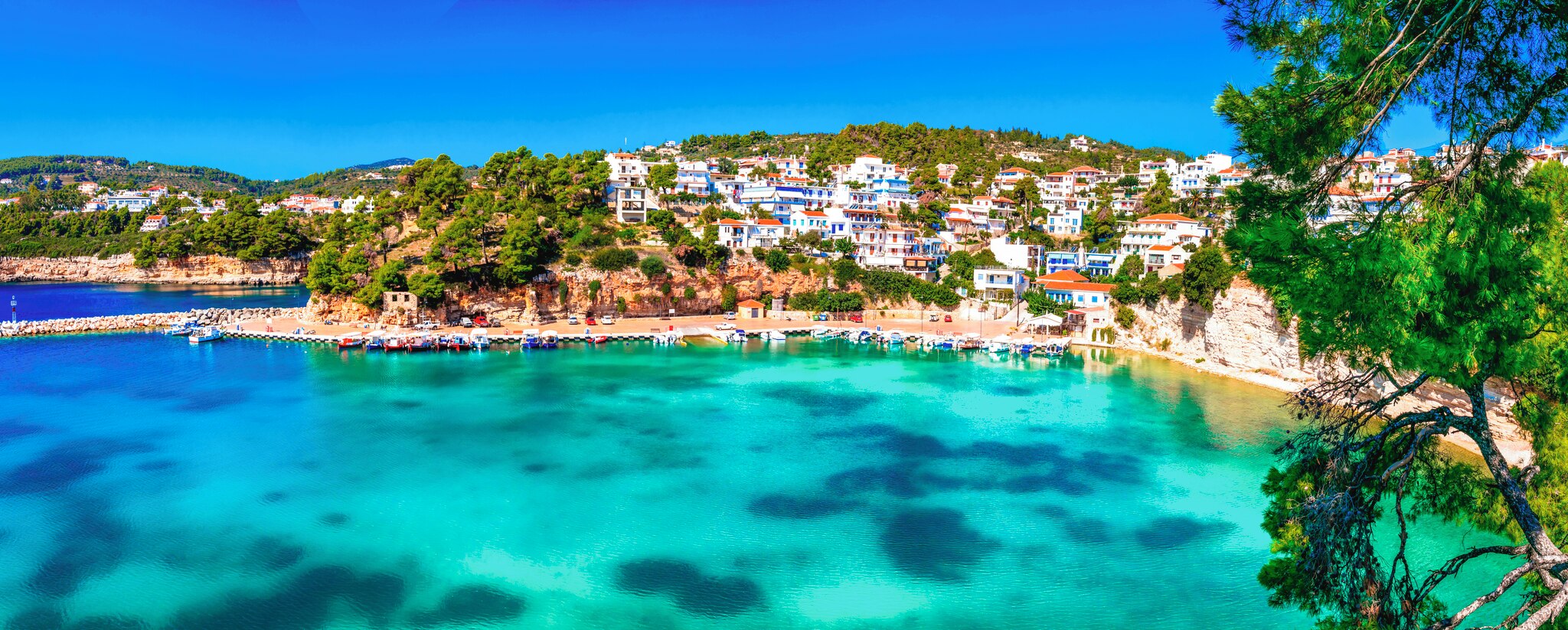 The coastal village of Votsi with clear turquoise waters, boats at the harbor, and white houses nestled among lush greenery.
