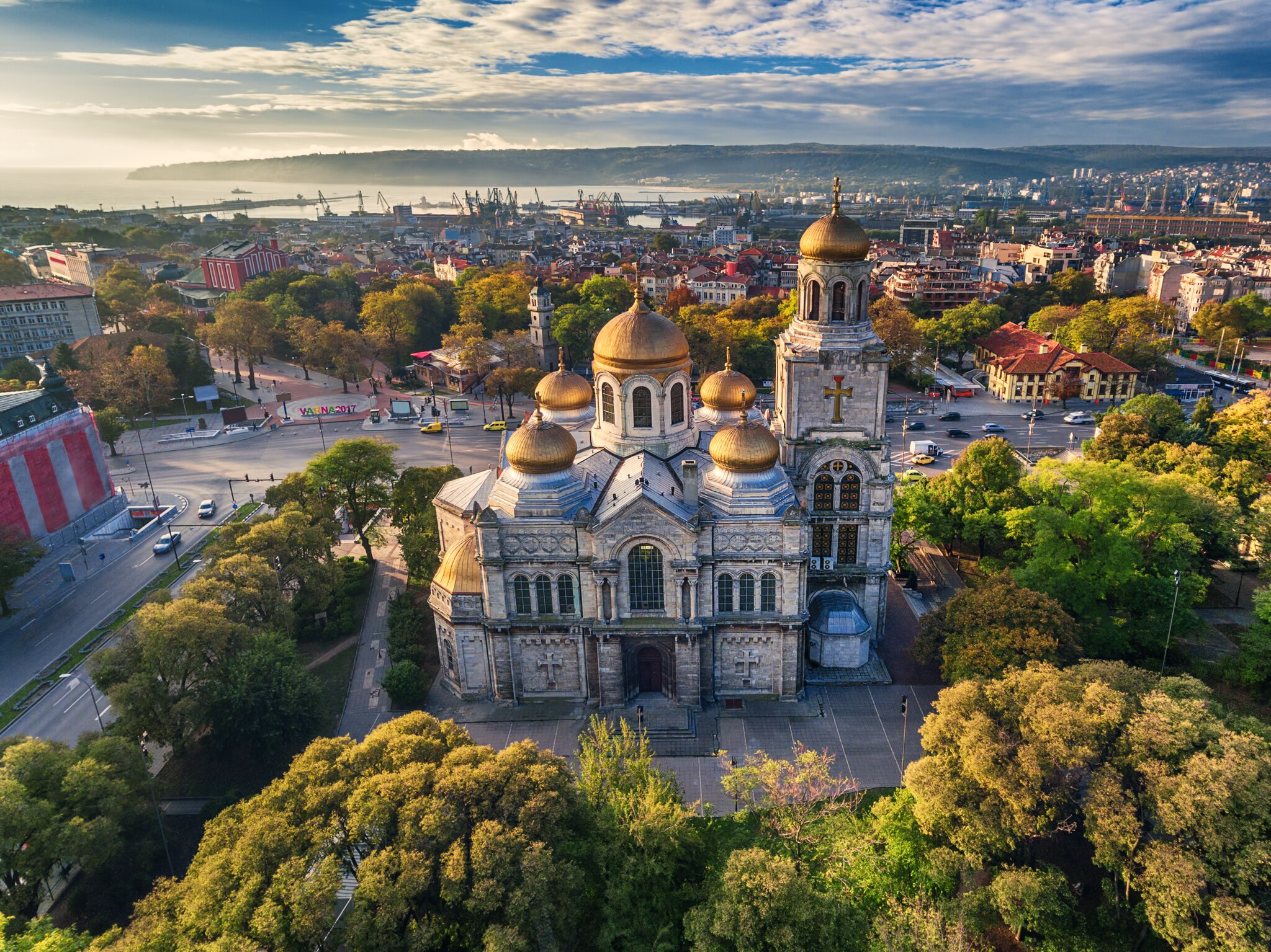 Aerial view of Varna showcasing the ornate domes of an iconic church amid trees and bustling city streets.