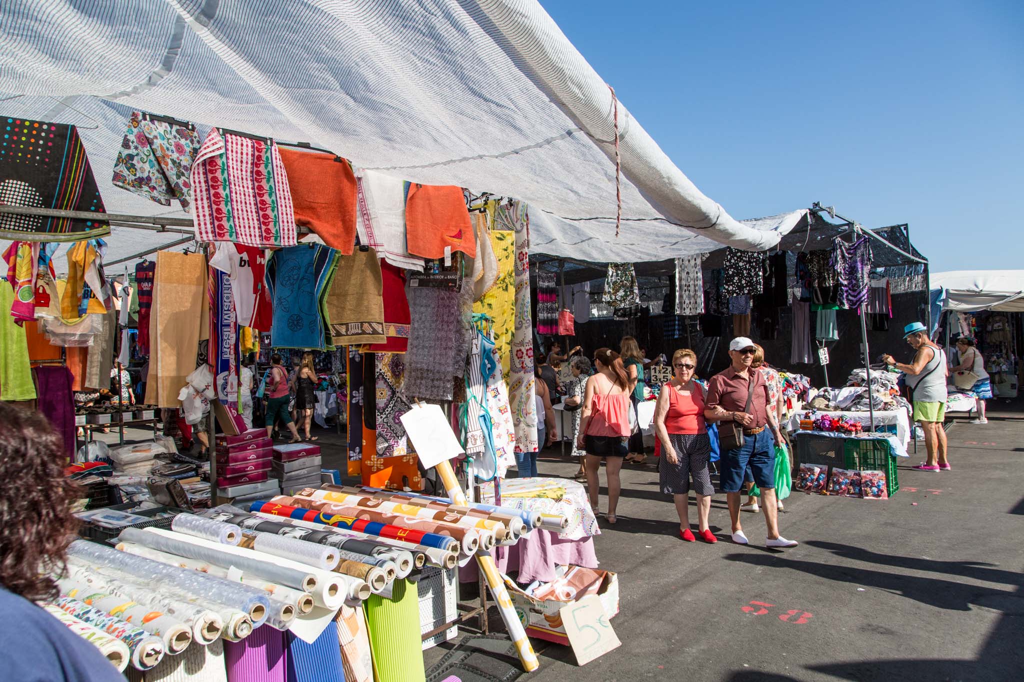 Vibrant scene at Old Town Market with colorful fabrics hanging above bustling shoppers exploring various vendor stalls.