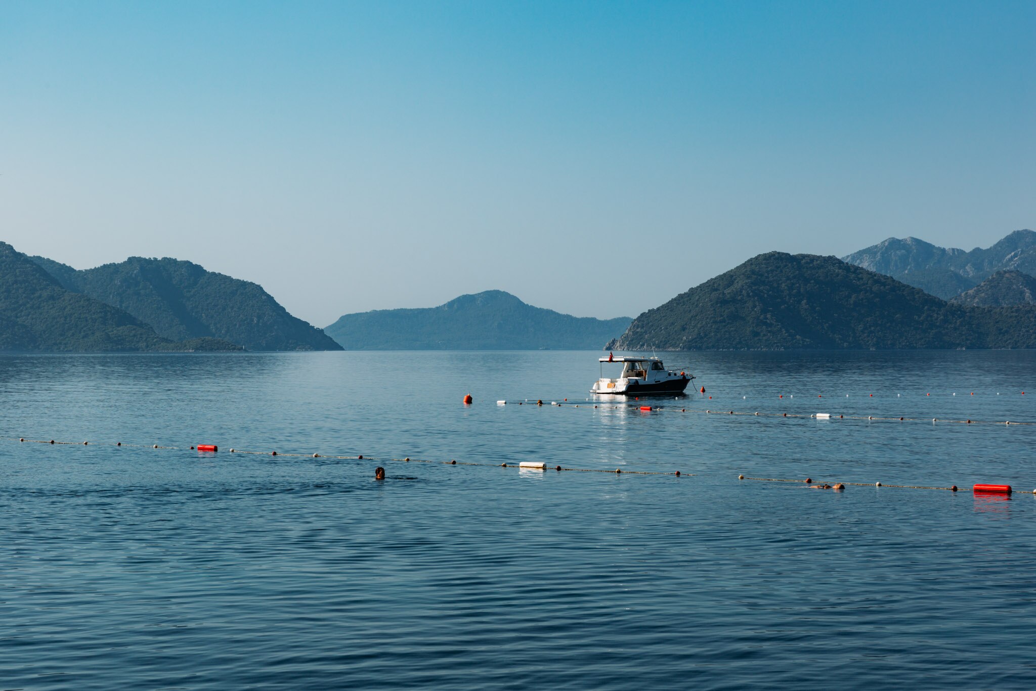 A serene view of Marmaris Beach featuring a small boat on calm waters, framed by distant mountains under a clear sky.