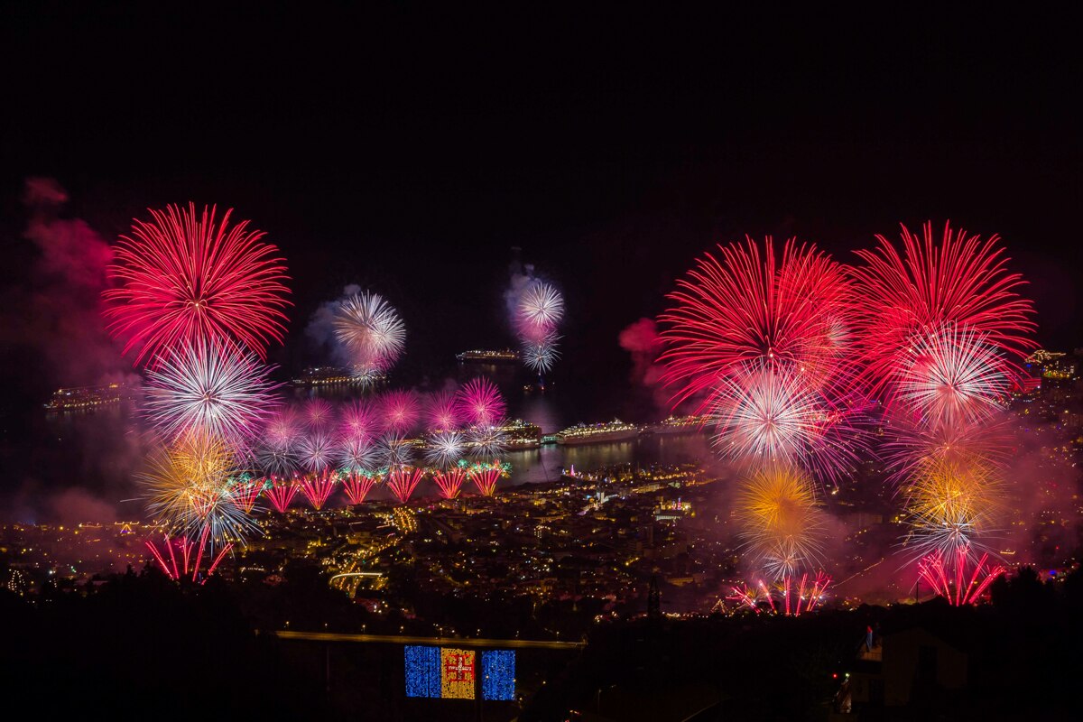 Fireworks illuminate the night sky over Madeira, celebrating Christmas and New Year with vibrant bursts of red, blue, and gold.