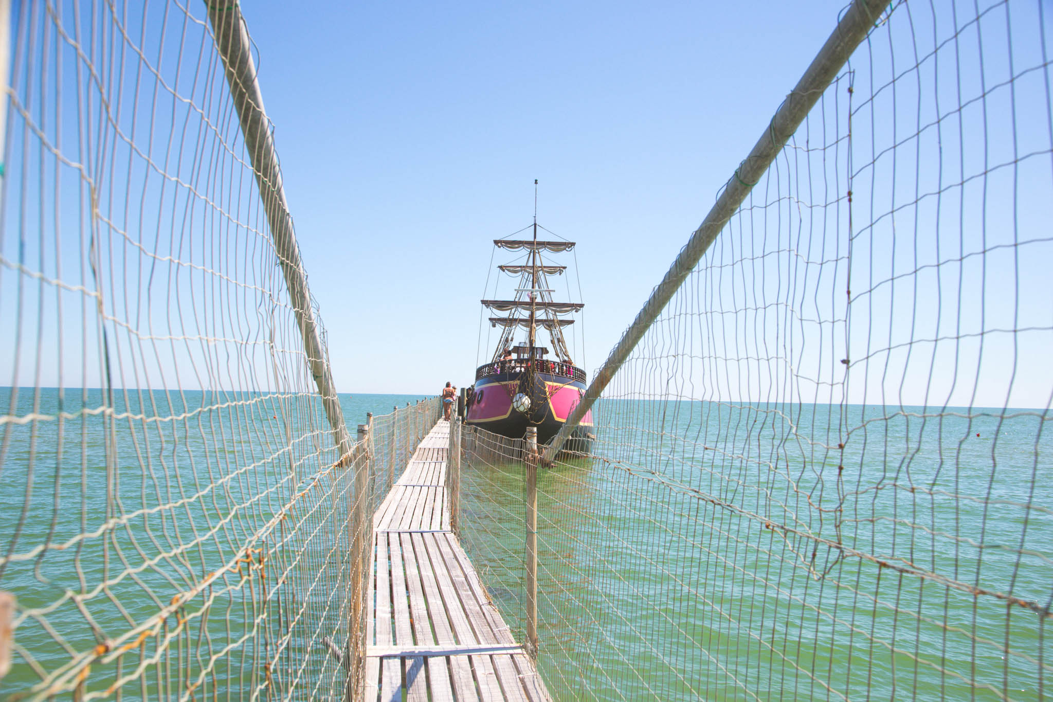 A pirate ship named Jolly Roger docked at a pier, with a clear blue sky and calm sea in the background.