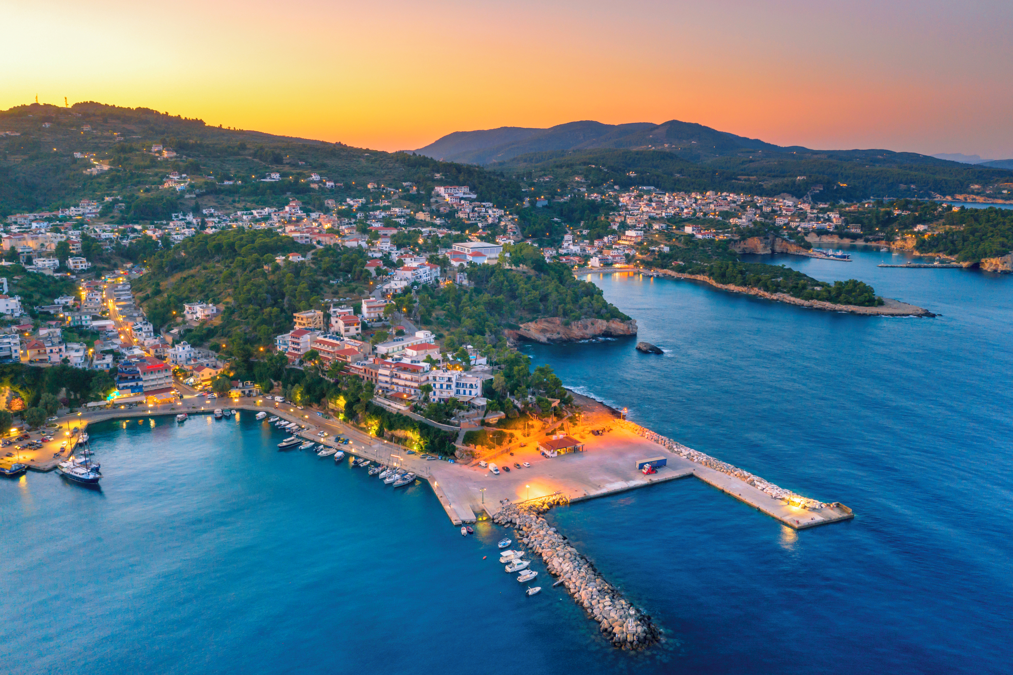 Stunning aerial shot of Patitiri, Alonissos, Greece at night, featuring the town illuminated against the deep blue sea.