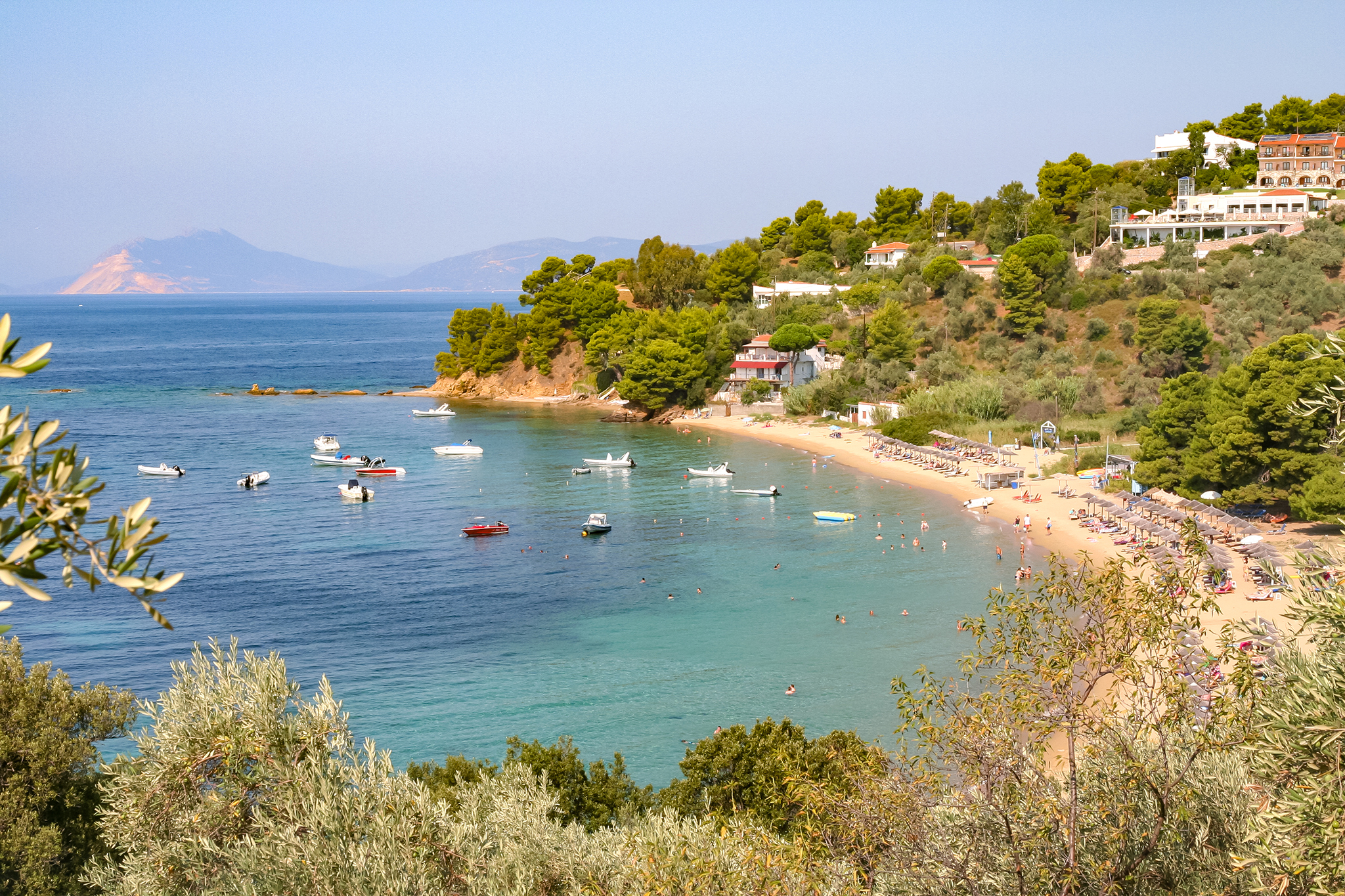 Troulos beach scene with boats anchored and people relaxing on the sandy shore.