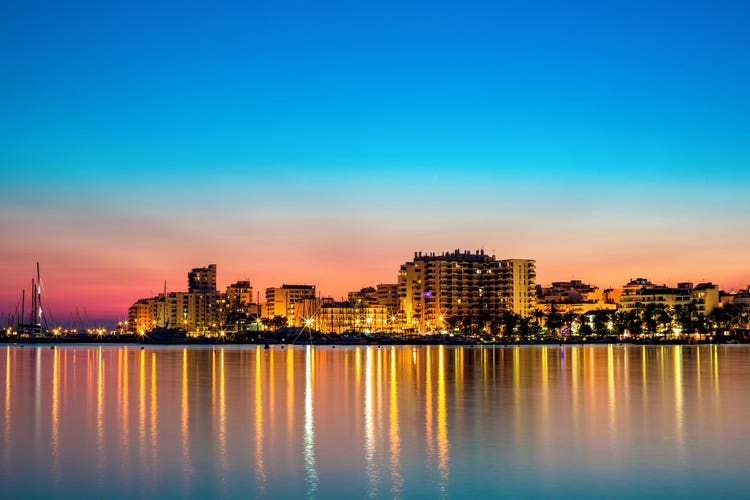 A sunset skyline of San Antonio, showcasing illuminated buildings along the waterfront and a serene gradient of colors in the sky.
