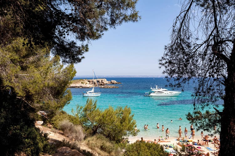 Boats gently bob in the ocean near Illetas' shoreline, framed by trees and rocky formations in the background.