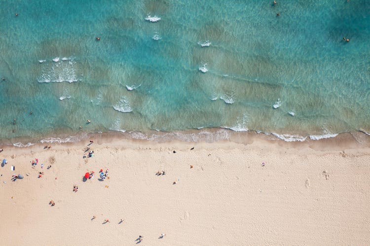 Aerial view of Colonia Sant Jordi beach, featuring crystal clear water, sandy shoreline, and beachgoers enjoying the sun.