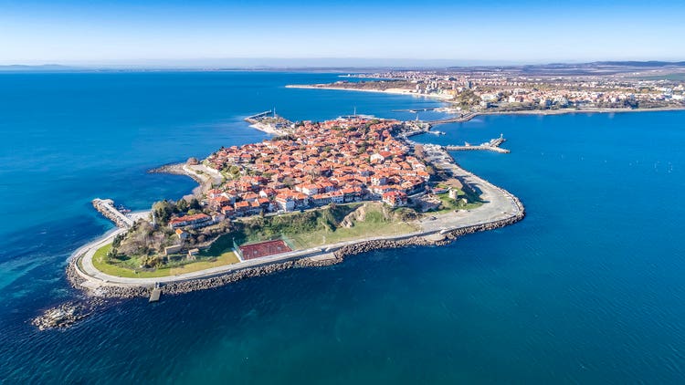Aerial view of Nessebar, Bulgaria, showcasing its red-roofed buildings surrounded by blue waters and green coastline.