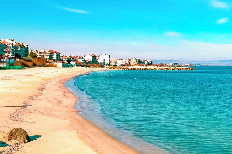 A scenic view of Pomorie's sandy beach and turquoise water, with colorful buildings lining the shore