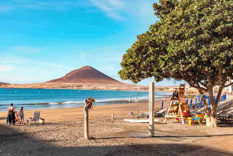 A picturesque landscape of El Medano beach, showcasing a volcanic mountain and the expansive ocean in front.