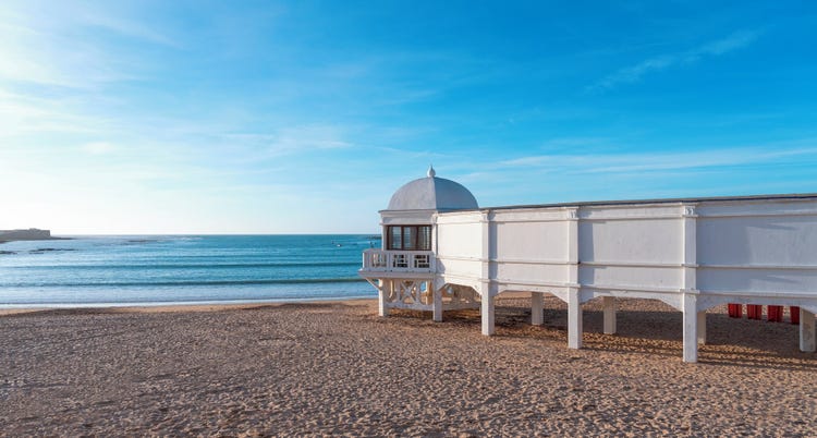 A white pavilion overlooking calm blue waters under a clear sky on a beach in La Caleta.