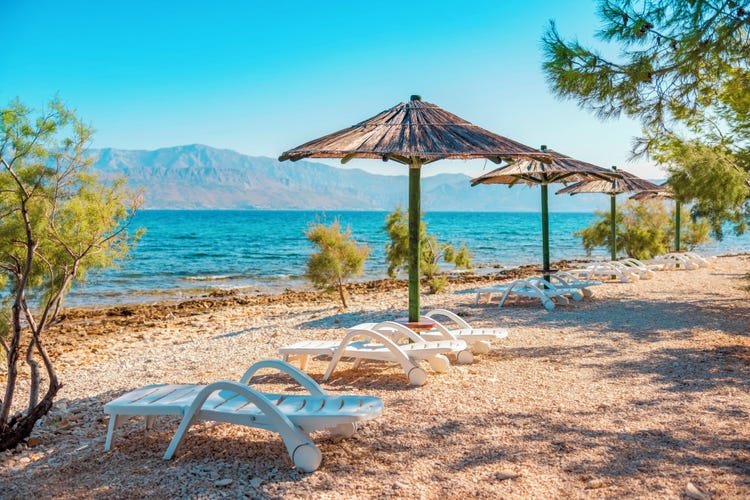 Beachfront scene at Brac Island featuring shaded loungers and clear blue waters with mountains in the background.