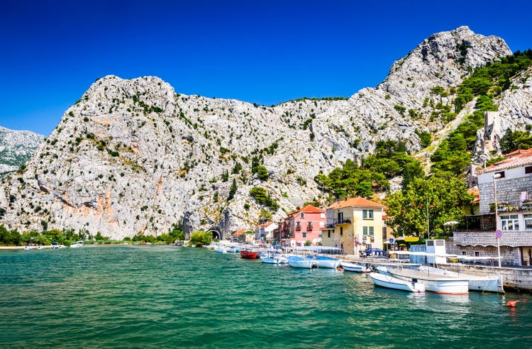 Scenic view of Omis, Croatia, featuring colorful houses against a backdrop of towering rocky cliffs and lush greenery.