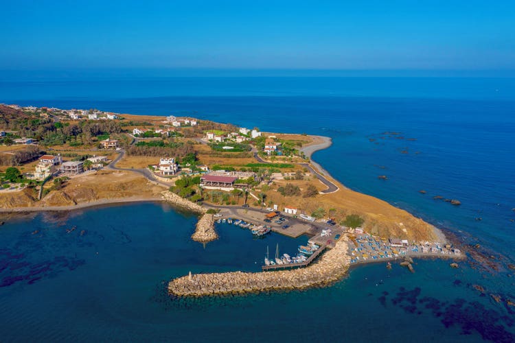 Aerial view of Pomos, showcasing coastal homes, a marina, and the azure sea under a clear sky.