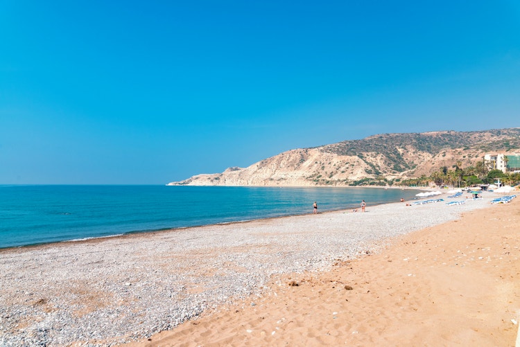 A sunny summer day at Pissouri beach, with people enjoying the sandy shores and clear blue waters, framed by distant hills.