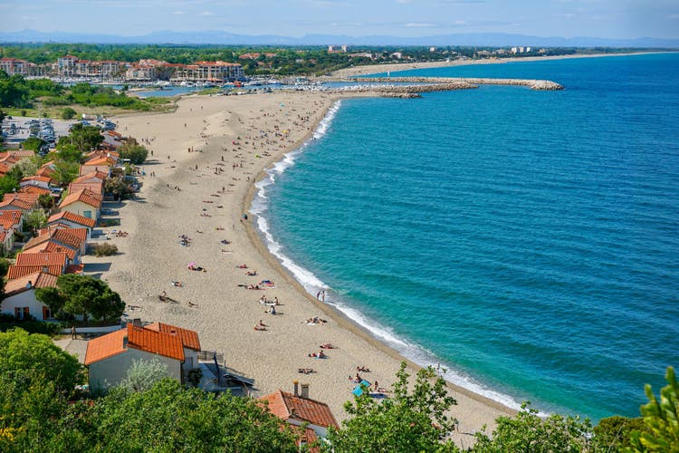 Sandy Mediterranean beach Le Racou in Argeles sur Mer with its old fishermen houses and the harbor in background, Roussillon, Pyrenees Orientales, France