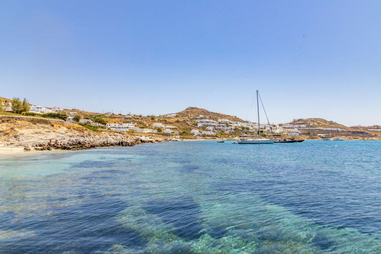 A Agios Ioannis beach, featuring rocky shores, crystal-clear waters, and picturesque white-washed buildings on a hillside.