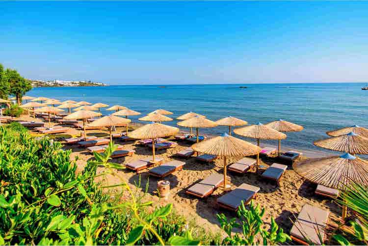 Stunning beach scene in Stalis featuring rows of sunbeds under thatched umbrellas, with coastline in the background.