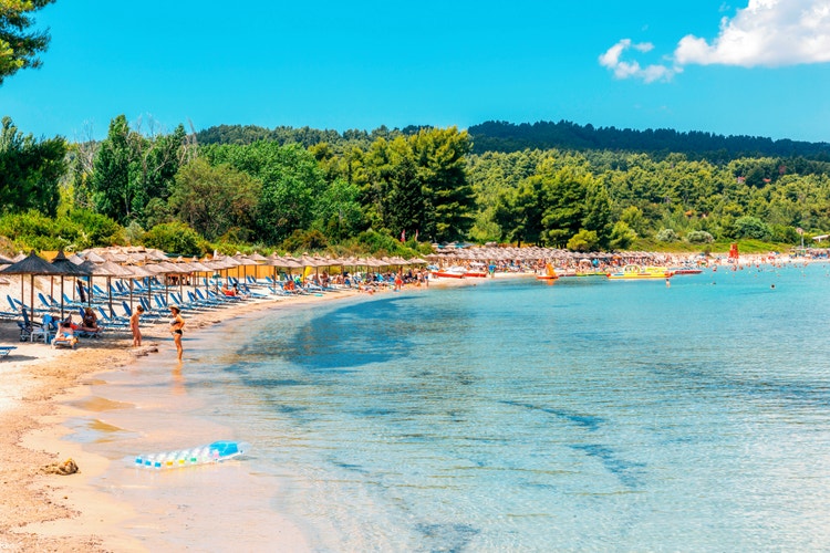 A serene beach in Paliouri featuring colorful umbrellas and chairs arranged along the sandy shore, and clear blue waters.