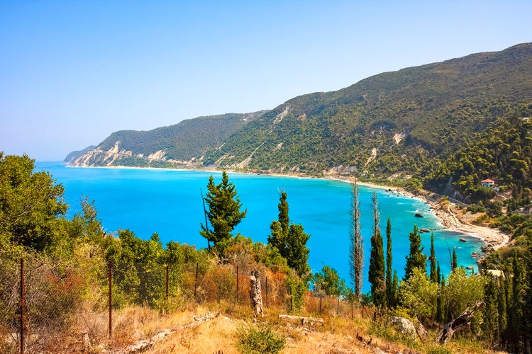 Scenic view of Tsoukalades with turquoise waters, lush greenery, and hills in the background under a clear blue sky.