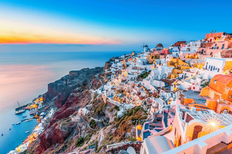 Whitewashed buildings in Firostefani in Santorini, on cliffs overlooking the tranquil aegean sea at sunset.