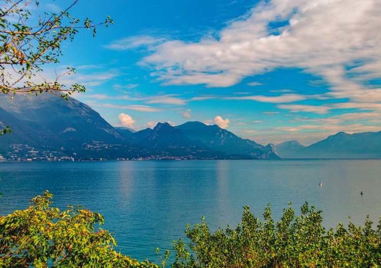 Scenic view of San Felice del Benaco, showcasing mountains and tranquil waters under a blue sky with scattered clouds.
