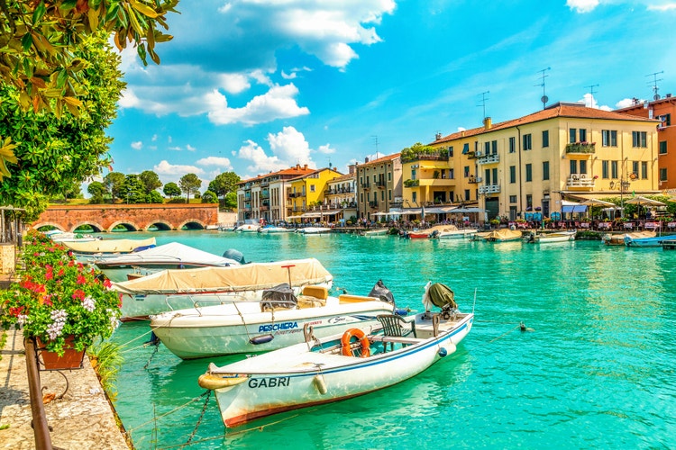 Peschiera's canal, with charming boats and colourful buildings along the waterway and a bridge in the background.