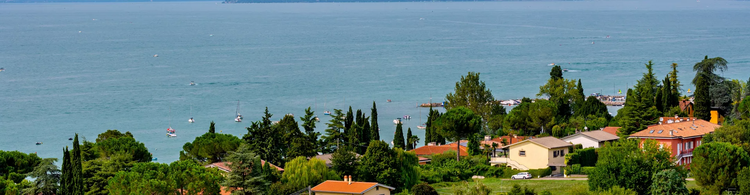 Panoramic view of Castelnuovo del Garda, featuring lush greenery, colorful houses, and boats on the serene lake waters.