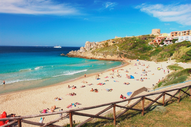 A sunny beach in Santa Teresa Gallura with people relaxing on the sand and a turquoise sea in the background.