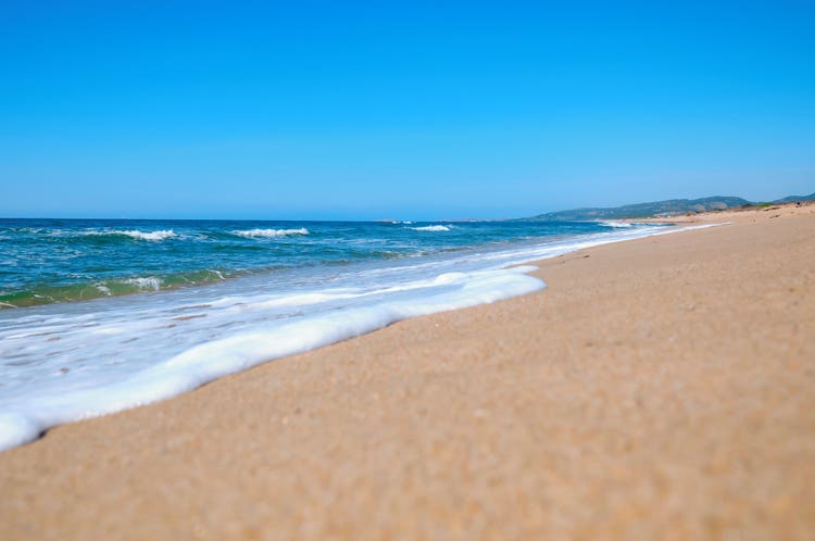 A picturesque beach in Li Cuncheddi with golden sand and rolling waves under a clear blue sky.