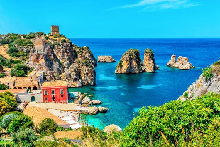 A coastal view of Scopello, featuring colorful buildings, rocky formations, and crystal-clear turquoise waters.
