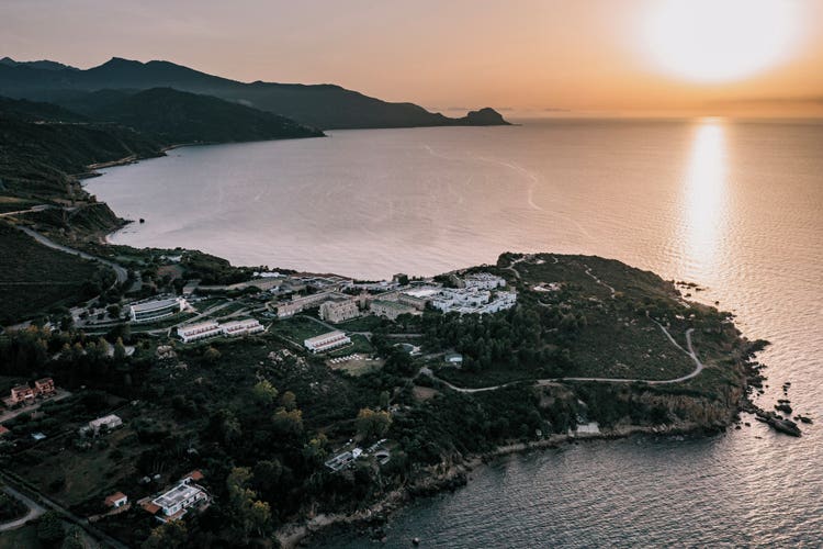 Aerial view of Pollina, coastal landscape under a sunset sky. Scenic greenery and buildings are visible.