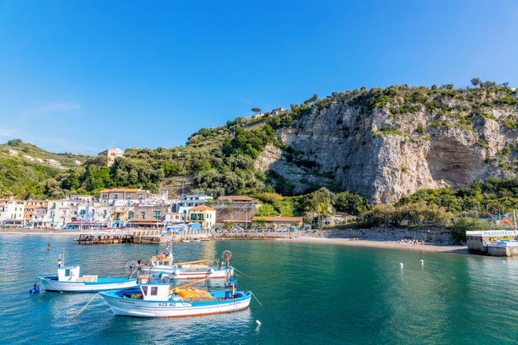 Scenic view of Massa Lubrense, featuring colorful seaside buildings, lush greenery, and towering cliffs under a clear sky.