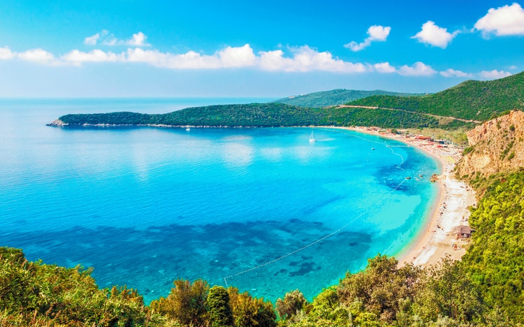 A stunning aerial view of Budva's coastline, featuring turquoise waters, beaches, and lush green hills under a clear sky.
