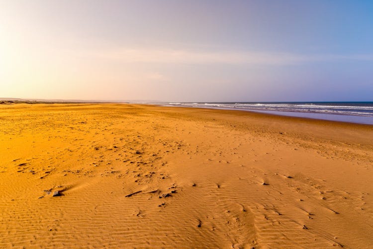 A serene view of Imi Ouaddar beach, featuring golden sands and gentle ocean waves under a soft, hazy sky.