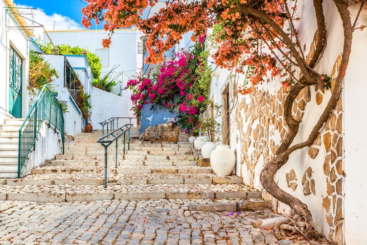 Charming stairway in Estoi, adorned with vibrant bougainvillea, rustic stone walls, and elegant pottery.