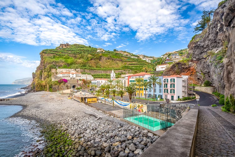 Scenic view of Ponta do Sol, Madeira, featuring coastal homes, palm trees, and lush green hills against a blue sky.
