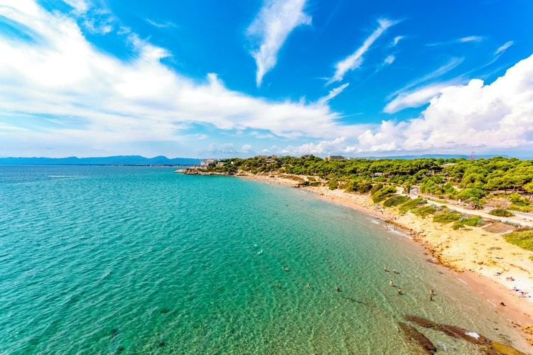 A scenic view of Cap Salou, showcasing turquoise waters, sandy beaches, and lush greenery all along the coastline.