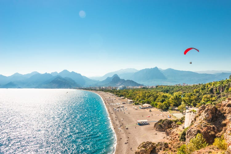 A paraglider soars gracefully over the stunning mountains and beach of Antalya, showcasing the beauty of the landscape.