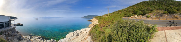 Panoramic view of serene turquoise waters and hills at Yaliciftlik, with rocky shoreline and a distant boat on the horizon.