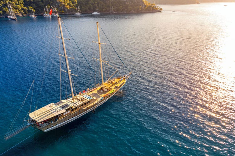 A wooden sailing yacht moored in the sparkling blue waters of Göcek, Turkey, with sunlight reflecting on the surface.