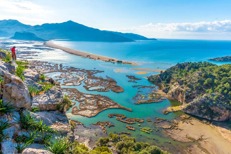 A panoramic view of Dalyan's turquoise waters and unique shoreline, framed by lush greenery and rocky cliffs.