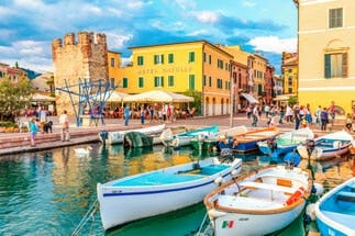Colourful harbour in Bardolino, Lake Garda, Italy with fishing boats, waterfront cafés and historic castle tower.