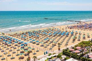 Wide view of a sunny beach lined with rows of colourful umbrellas and chairs at Lido di Jesolo on the Venetian Riviera, Italy.